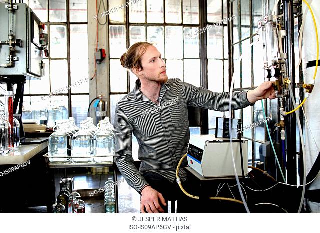 Young male vodka distiller adjusting valve in distillery workshop