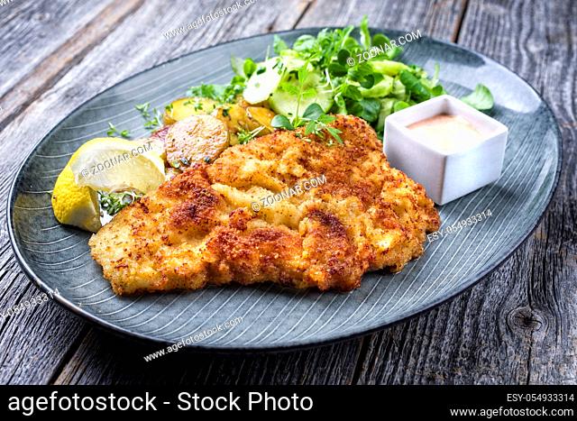 Fried Wiener schnitzel from veal topside with fried potatoes and lettuce as closeup modern design plate
