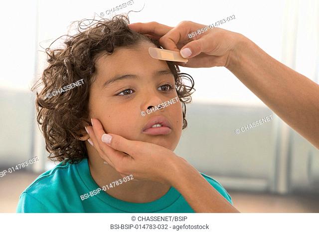Mother putting adhesive bandage on her son's forehead