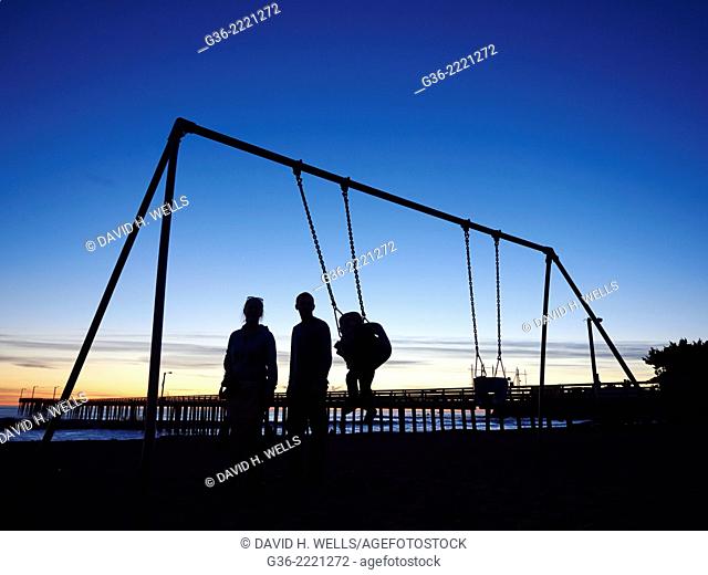 Silhouette of family at playground in front of pier, Cayucas, California, United States