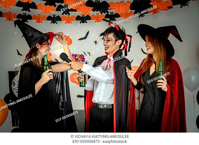 Group of young adult and teenager people celebrating a Halloween party carnival Festival in Halloween costumes drinking alcohol beer singing a song and dancing