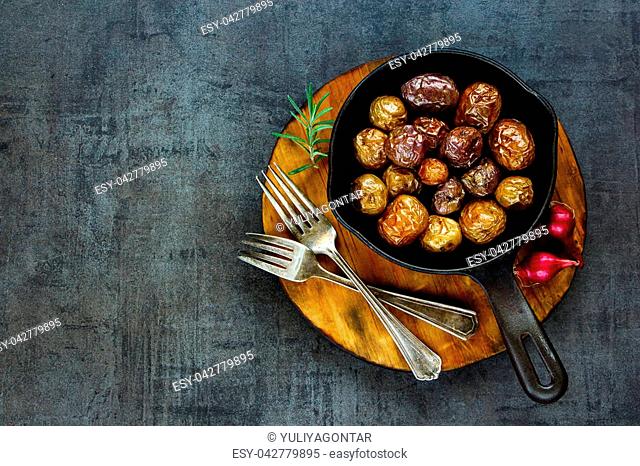 Fried baby potatoes in vintage cast iron pan on black concrete background, copy space. Healthy food concept. Overhead shot
