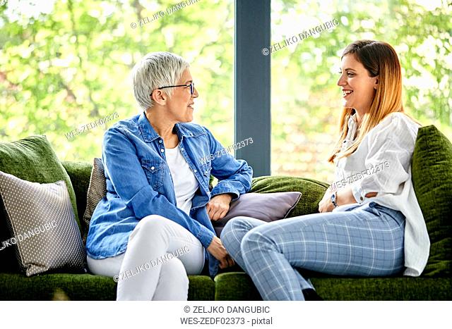 Mother and adult daughter sitting on couch, talking