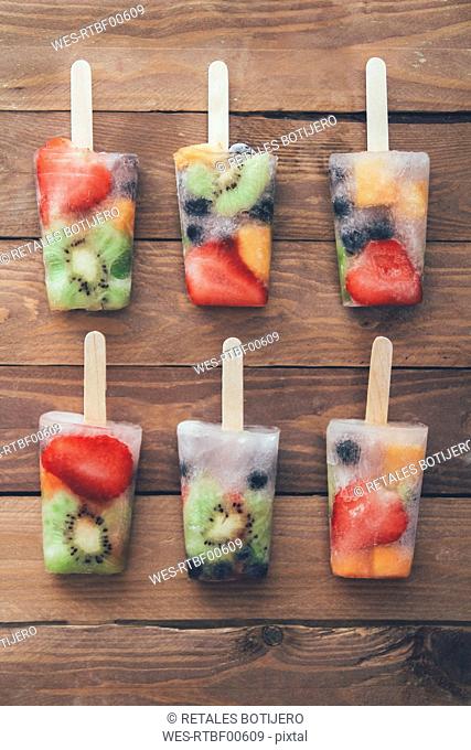Two row of six fruit ice lollies with fresh fruits on wood