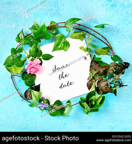 Save the Date, invitation design with a flat lay wreath of leaves and flowers, shot from the top on a blue background with ivy and rose
