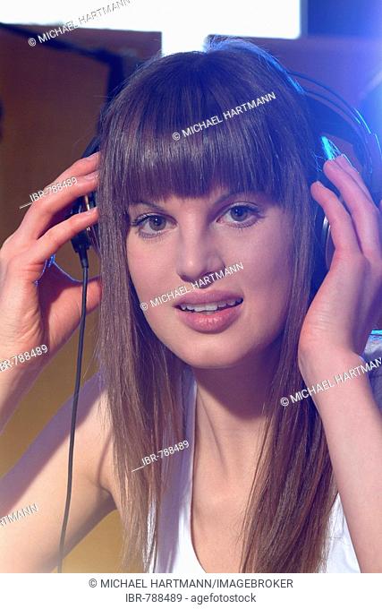 Portrait of a young woman with headphones at the mixing console in a recording studio