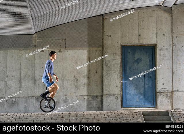 Teenager, 19 years old, rides unicycle, under bridge, Germany, Europe
