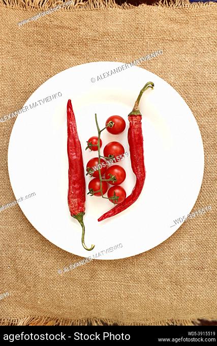 branch of red cherry tomatoes and two pods of chili peppers on the plate. Red vegetables on the sacking