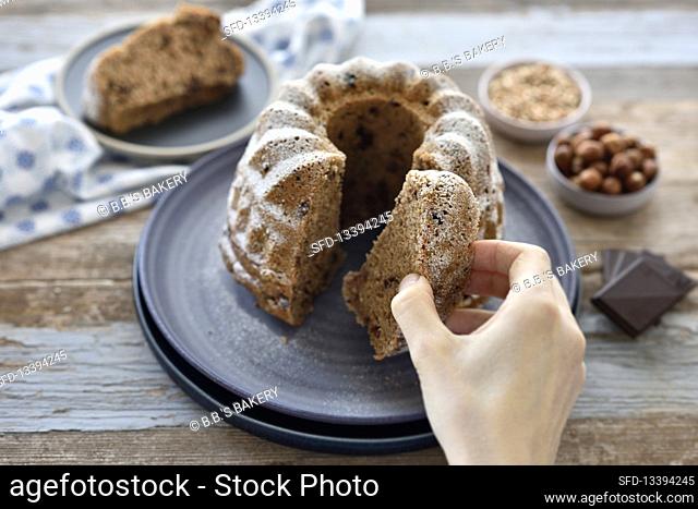 Vegan hazelnut chocolate bundt cake - a woman reaches for a slice of cake