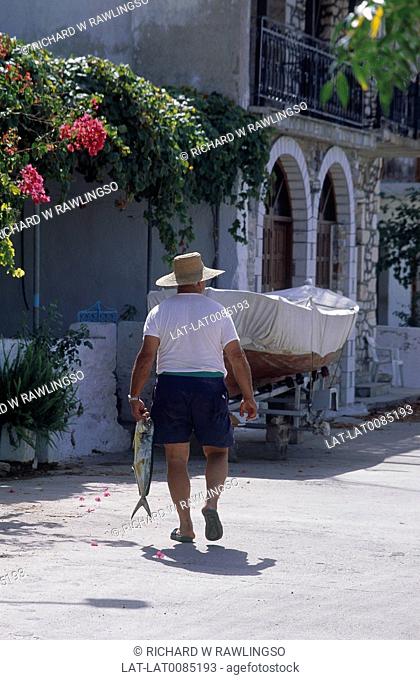 The Mani. Village street. Backview of man. Carrying large fresh fish. Boat parked on road. Bougainvillea