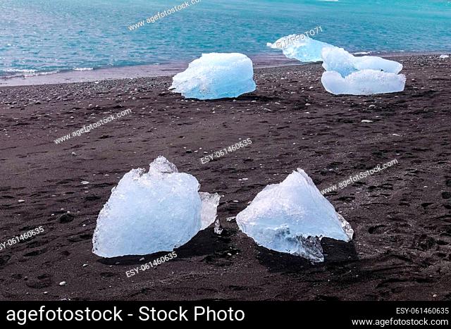 Diamond Beach in Iceland with blue icebergs melting on black sand and ice glistening with sunlight
