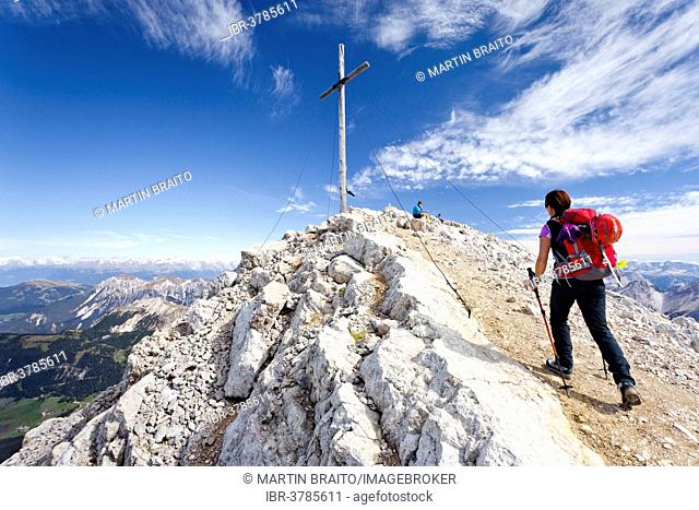 Mountaineer at the summit cross of Mt Heiligkreuzkofel of the Fanes Group in the Fanes-Sennes-Prags Nature Park, Val Badia below, Alta Badia, Dolomites