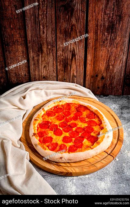 Homemade pizza with pepperoni lies on a wooden tray on a background of wooden boards. Daylight