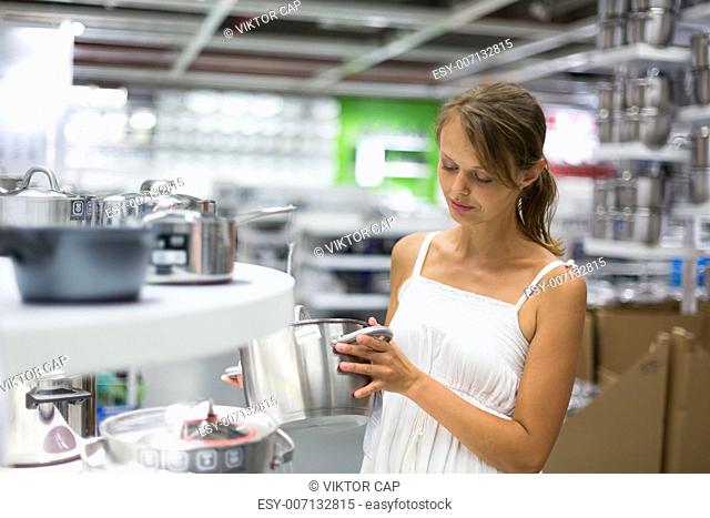 Pretty, young woman choosing a the right pot for her cooking in a modern home furnishings store (color toned image shallow DOF)