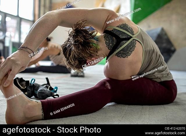 Young female rock climber stretching in climbing gym
