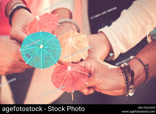 Close up women's hands together with umbrella cocktail for summer style concept and vacation in friendship colours and happiness with group of people enjoying...