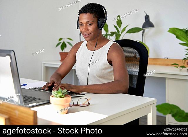 Female customer service representative wearing headphones working on laptop at office