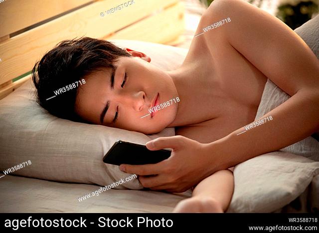 Young man lay on the bed to play mobile phone