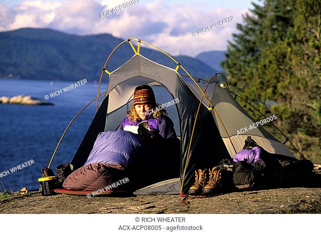 Woman reads a book in her tent, Lighthouse Park, West Vancouver, British Columbia, Canada