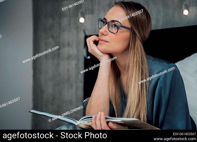 Portrait of a Beautiful Dreamy Woman with Photo Album Before Sleep. Wearing Glasses. Cozy Warm Evening at Home. Happy Life