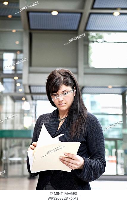 A young Caucasian businesswoman going through paperwork in a convention centre lobby area