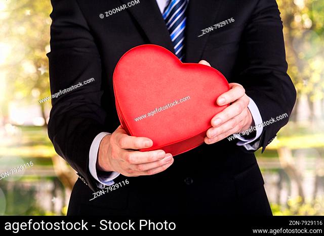 Young man holds red heart box on the autumn colors background