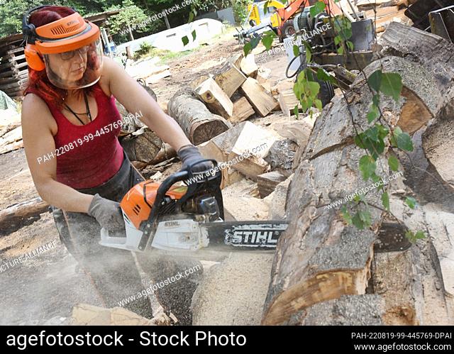 09 August 2022, Saxony, Eisenhammer: In her Eisenhammer charcoal workshop in the Düben Heath, charcoal burner Norma Austinat uses a chainsaw to cut beech logs...
