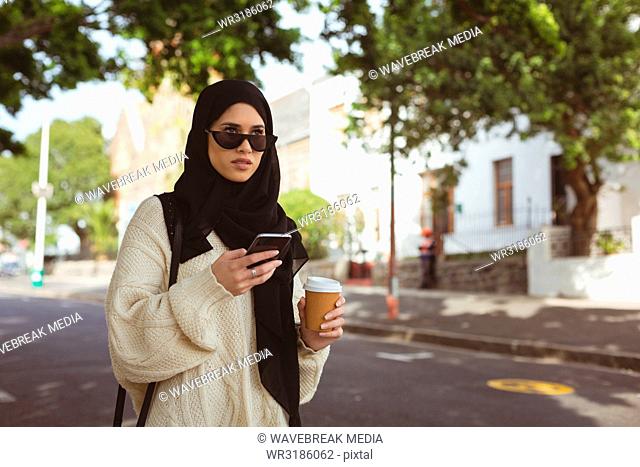 Hijab woman using mobile phone while holding coffee cup