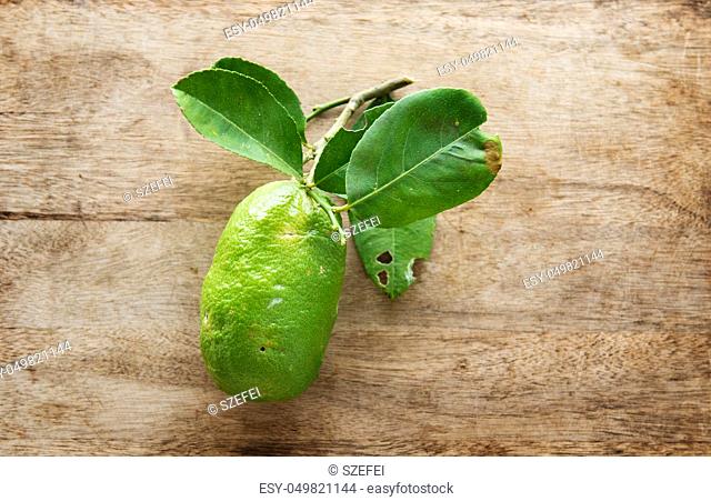 Top view fresh organic lemon with leaves on wooden table background, imperfect insect bites, pesticide free