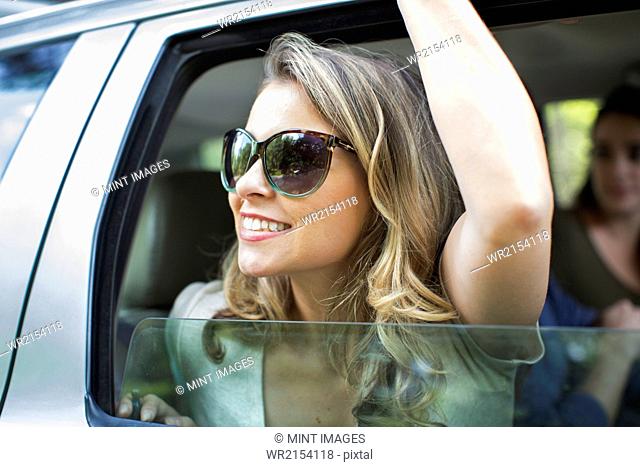 A young woman leaning out of a car window with her arm raised