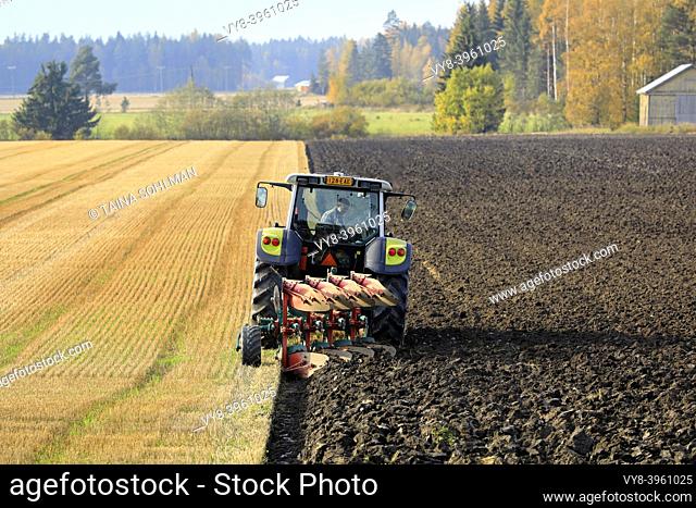 Farmer plows field with green Valtra tractor and plough on a beautiful day of autumn in South of Finland. Jokioinen, Finland. October 2, 2020