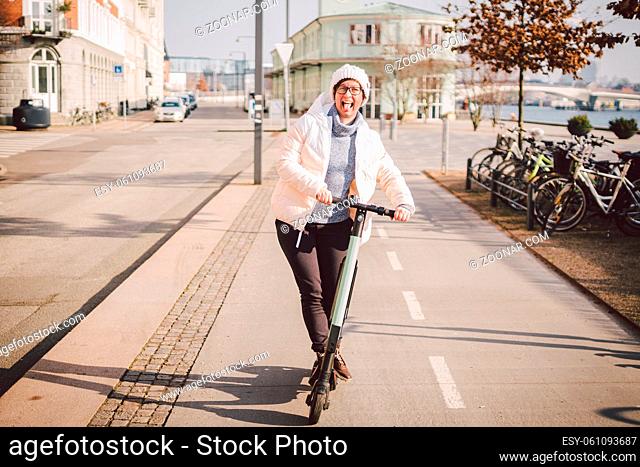 Young woman riding an electric scooter on bike path in copenhagen, modern girl, new generation, electric transport in city, ecology and ecological transport