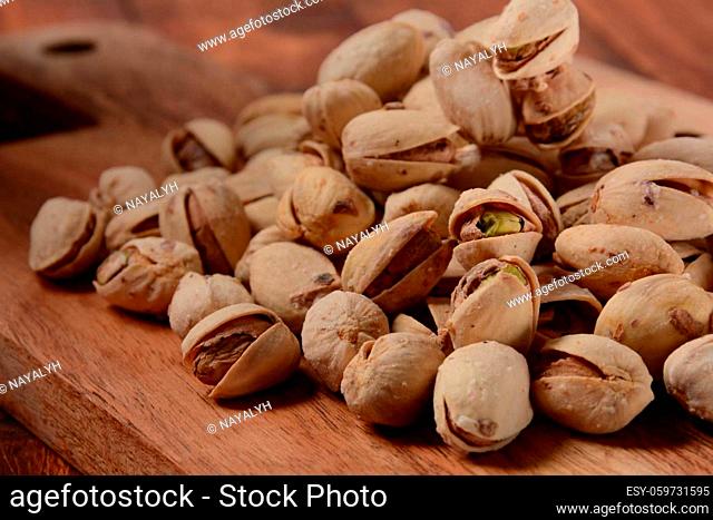 Pistachios on wooden surface, pile of pistachios, roasted pistachios in a bowl
