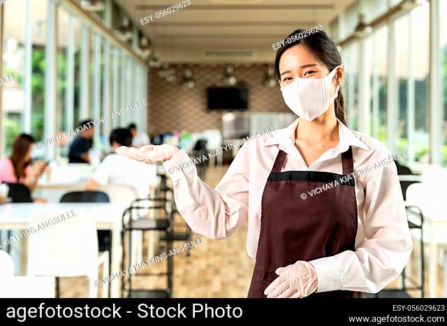 Portrait attractive asian waitress wear face with background of customers sit in social distance table in restaurant indoor