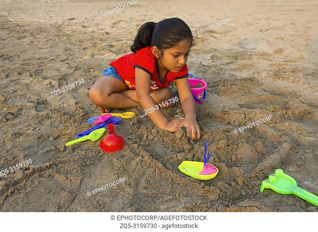 Little girl trying to make a fort with sand on Alibag beach, India