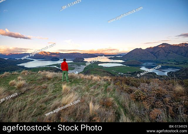 Walker looks out over Wanaka Lake and mountains at sunset, Rocky Peak, Glendhu Bay, Otago, South Island