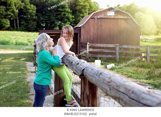 Caucasian grandmother and granddaughter smiling at farm fence