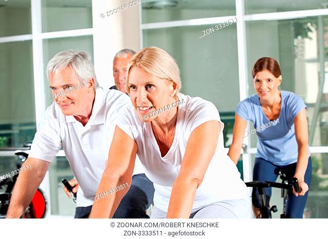 Glückliche Senioren auf Spinning-Rädern beim Reha-Training im Fitnesscenter