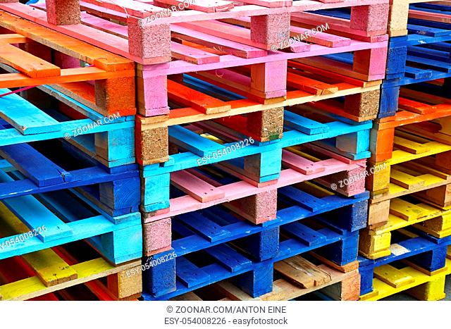 Close up stack of many vivid multicolor painted colorful wooden pallets, high angle diagonal view