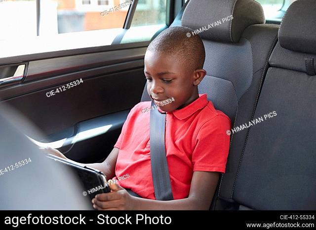 Boy using digital tablet in back seat of car