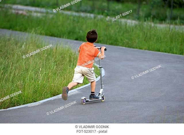 A young boy riding a push scooter along a path