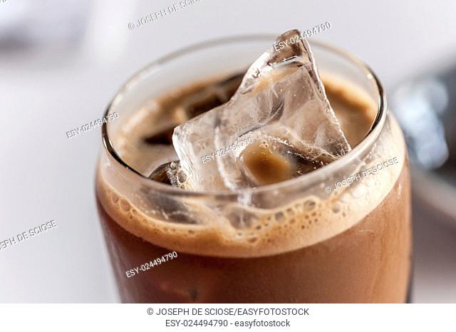 A close up of an ice cube on top of a glass of iced coffee