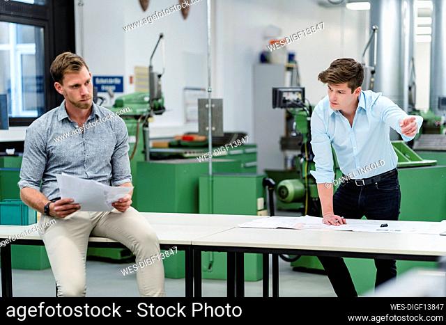 Businessman discussing business strategy with male engineer on desk in factory