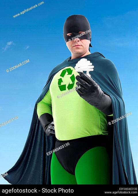 Eco superhero with green recycle arrow symbol on chest holding CFL bulb standing over blue sky - Energy saving concept