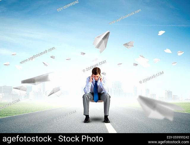 Businessman is sitting on an office chair with his head in his hands. Paper planes fly around