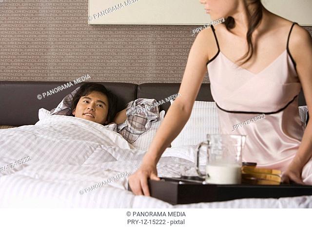 Husband sleeping in bed, wife taking a tray of breakfast aside