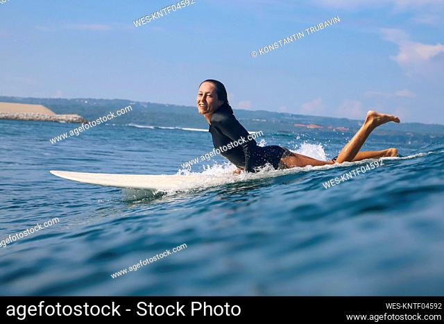 Happy woman lying on surfboard in the sea, Bali, Indonesia