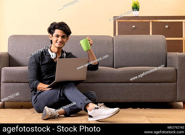 Teenage boy using laptop while sitting on floor in living room