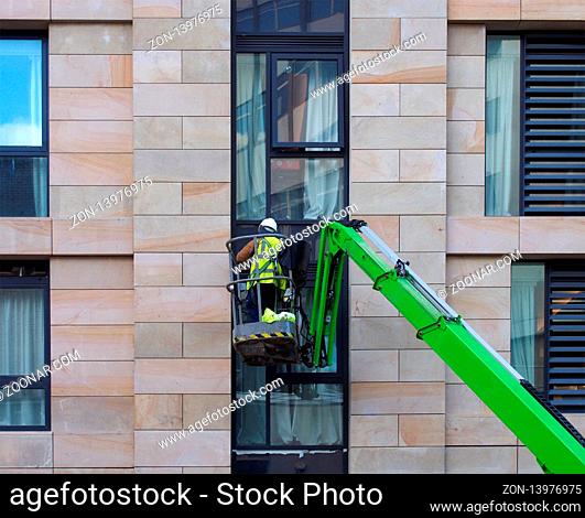an unidentifiable construction worker in a green aerial work platform on a large housing urban construction site
