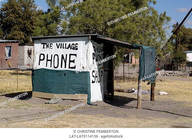 Collection of buildings. Houses. Homes. Small concrete shack painted green and white. Huge black signs. The Village Phone Shop. Communication